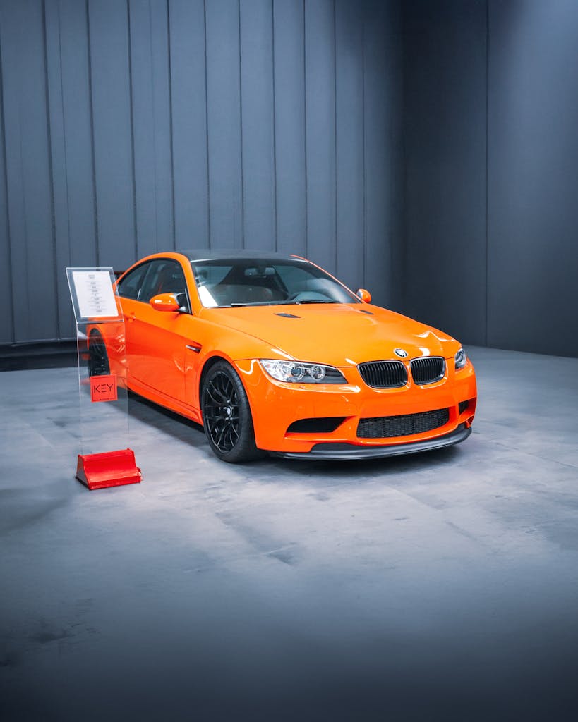Capture of a striking orange BMW M3 on display indoors in a modern showroom.